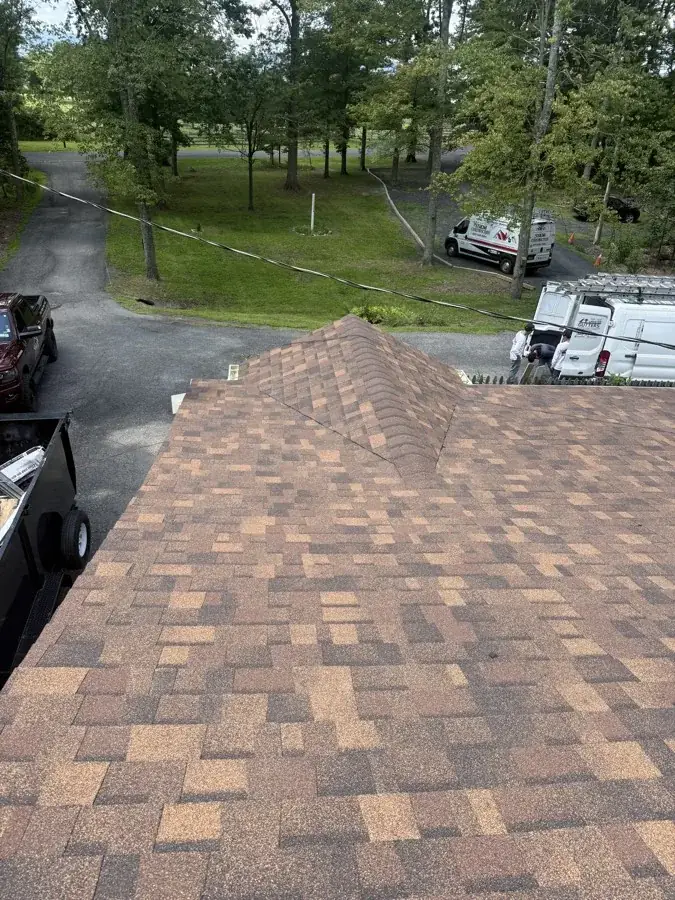 Aerial view of a finished shingle roof hip and ridge, with the SSKM Construction van parked below